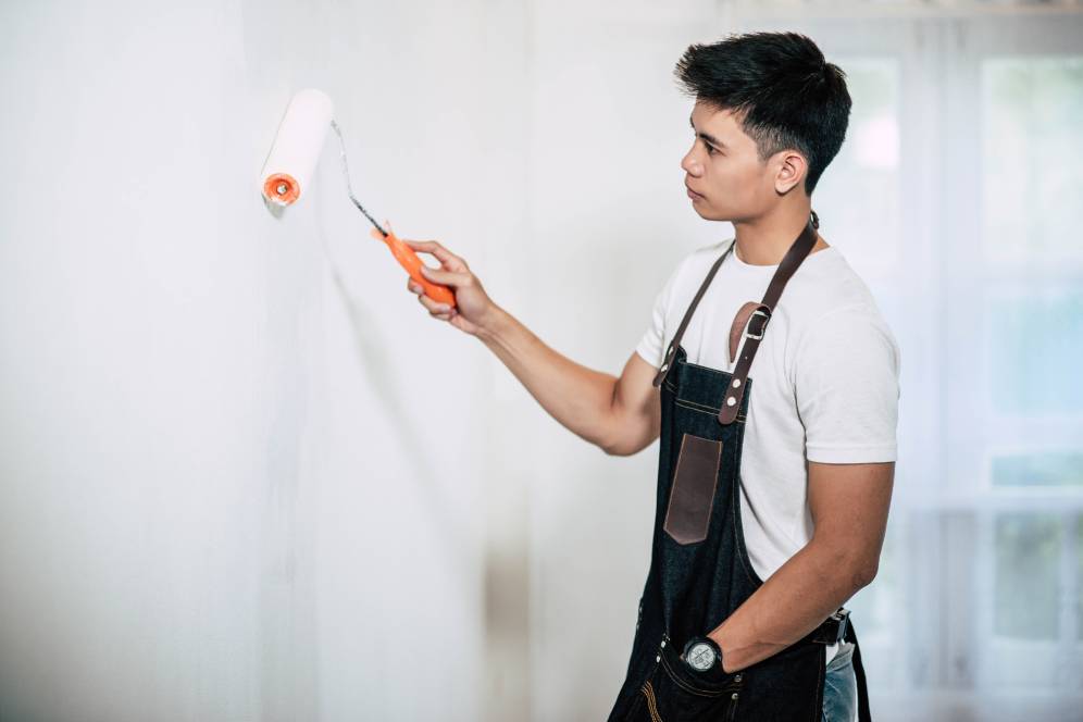 Person in a white shirt and apron painting a wall with a roller